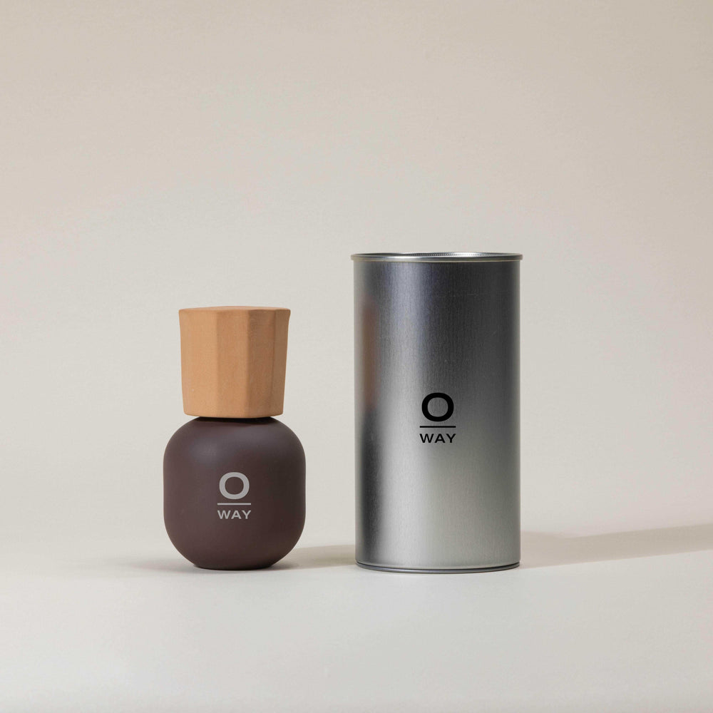 Flacone marrone con logo Oway di profumo iconico con tappo in terracotta. Accanto al flacone latta da confezione in alluminio grigia con logo Oway