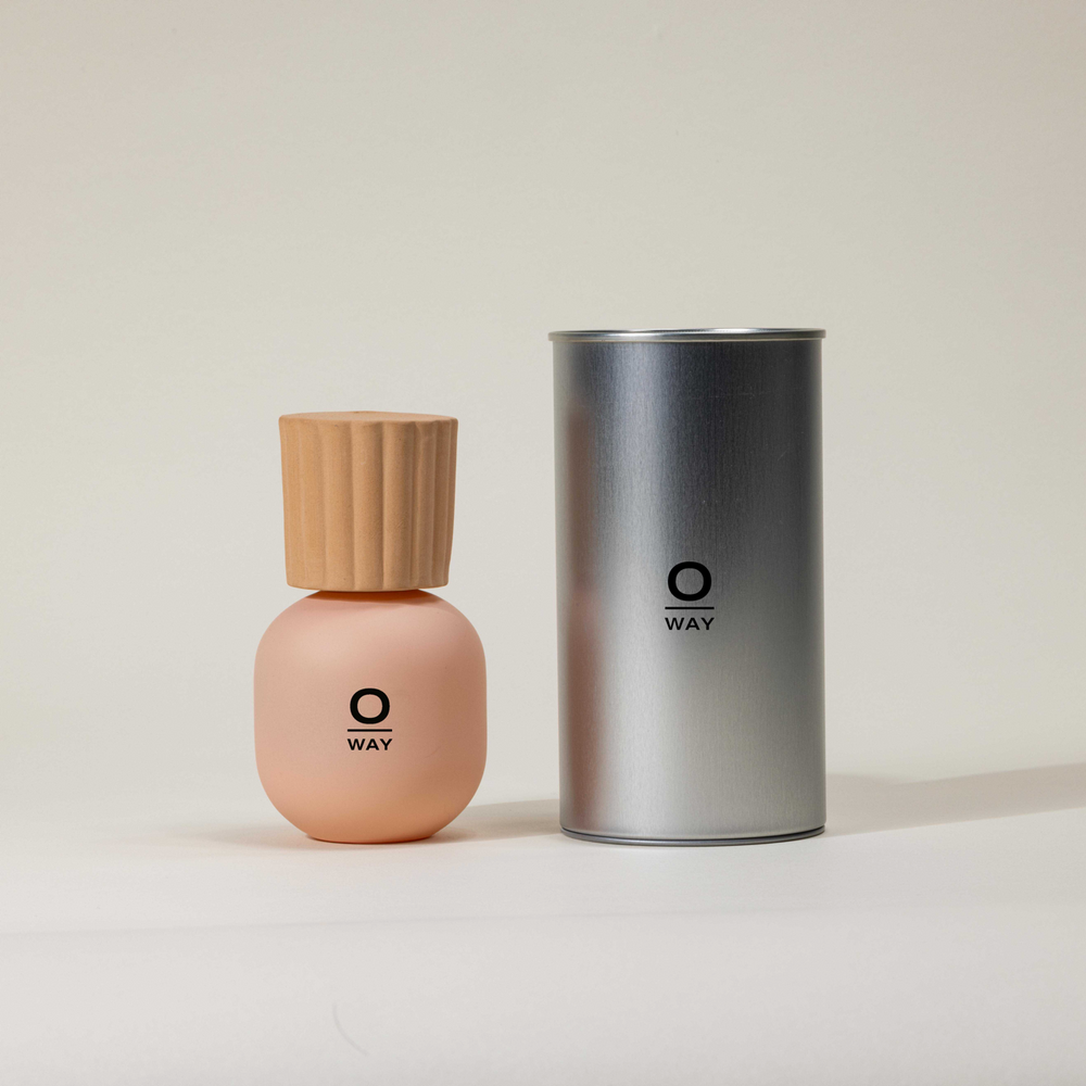 Flacone rosa con logo Oway di profumo iconico con tappo in terracotta. Accanto al flacone latta da confezione in alluminio grigia con logo Oway